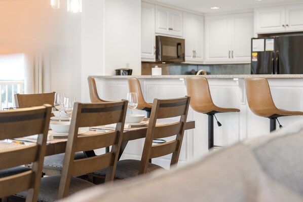 A modern kitchen with white cabinets, a stainless steel refrigerator, and a dining area with wooden chairs and a table set for a meal.