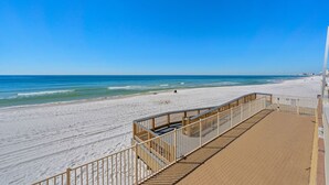 A beach with a wooden boardwalk leading to the shore, clear blue sky, and calm sea.