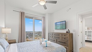 A hotel room with a large bed, a ceiling fan, a television, and a view of the city.