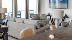Una sala de estar con un sofá gris, una mesa de comedor y un televisor que muestra una escena de playa.