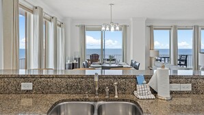 Una cocina con encimeras de granito, fregaderos de acero inoxidable y vistas al océano a través de amplios ventanales.
