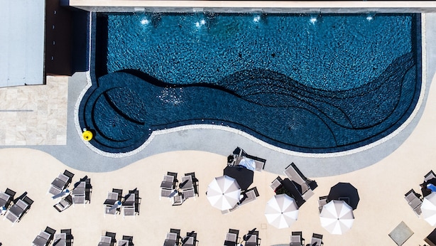 An aerial view of a pool with a wavy edge, surrounded by sun loungers and umbrellas. - Hotel Baffo Rosso (Corropoli)