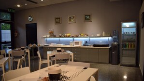A modern kitchen with white appliances, a refrigerator, and a dining area with white chairs and tables. - Hotel Baffo Rosso (Corropoli)