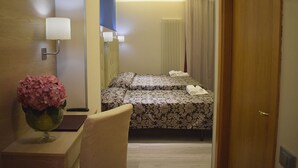 A hotel room with two beds, a bedside table with a vase of flowers, a lamp, and a view of the hallway. - Hotel Baffo Rosso (Corropoli)