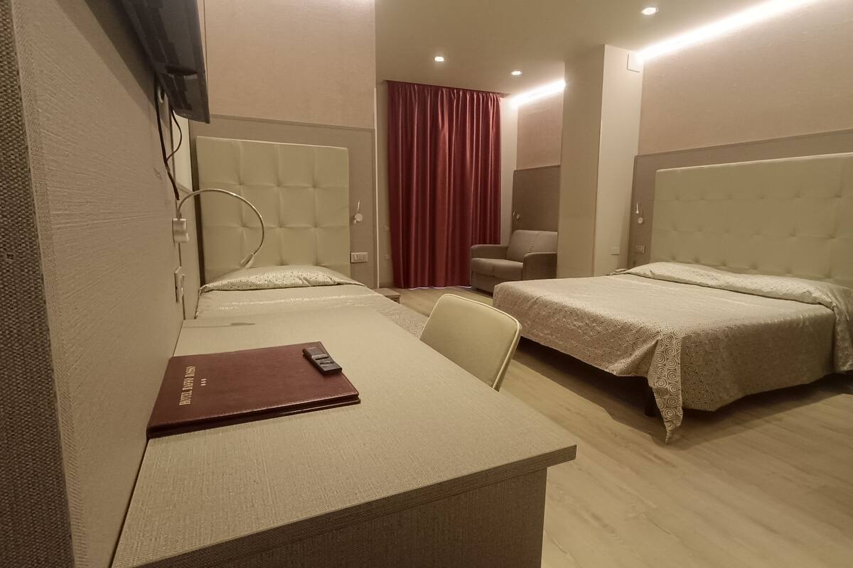 A hotel room with two beds, a desk, a chair, a TV, and a red curtain.