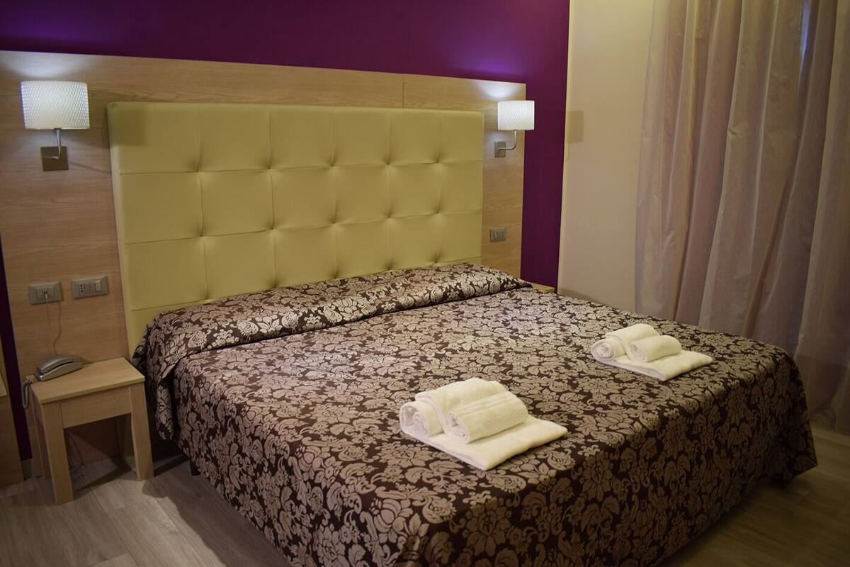 A hotel room with a large bed, a bedside table, a lamp, and a curtain.