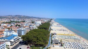 A coastal cityscape with a beach lined with umbrellas and sun loungers, buildings with balconies, and a clear blue sky. - Hotel Baffo Rosso (Corropoli)