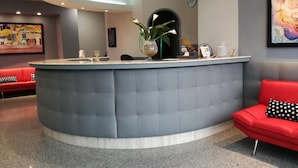 A reception area with a curved grey counter, a red sofa, and a painting on the wall. - Hotel Baffo Rosso (Corropoli)