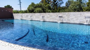 A swimming pool with clear blue water, a stone wall, and a building in the background. - Hotel Baffo Rosso (Corropoli)