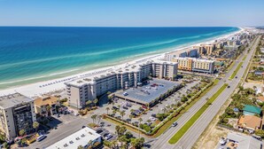 An aerial view of a coastal hotel with a beachside location, multiple parking lots, and a road running parallel to the beach.