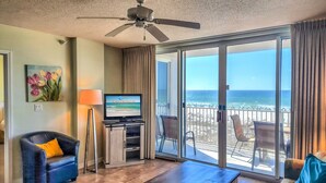A hotel room with a balcony, a television, a ceiling fan, and a view of the ocean.
