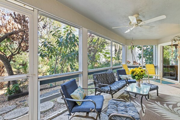 A covered patio with outdoor furniture, large windows, and a ceiling fan.