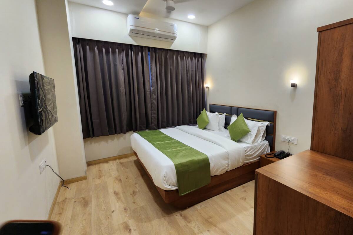 Habitación de hotel con una cama, una mesita de noche de madera, un equipo de aire acondicionado, un televisor montado en la pared y un armario de madera.