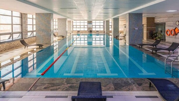 An indoor swimming pool with clear lanes, lounge chairs, and a tiled floor.