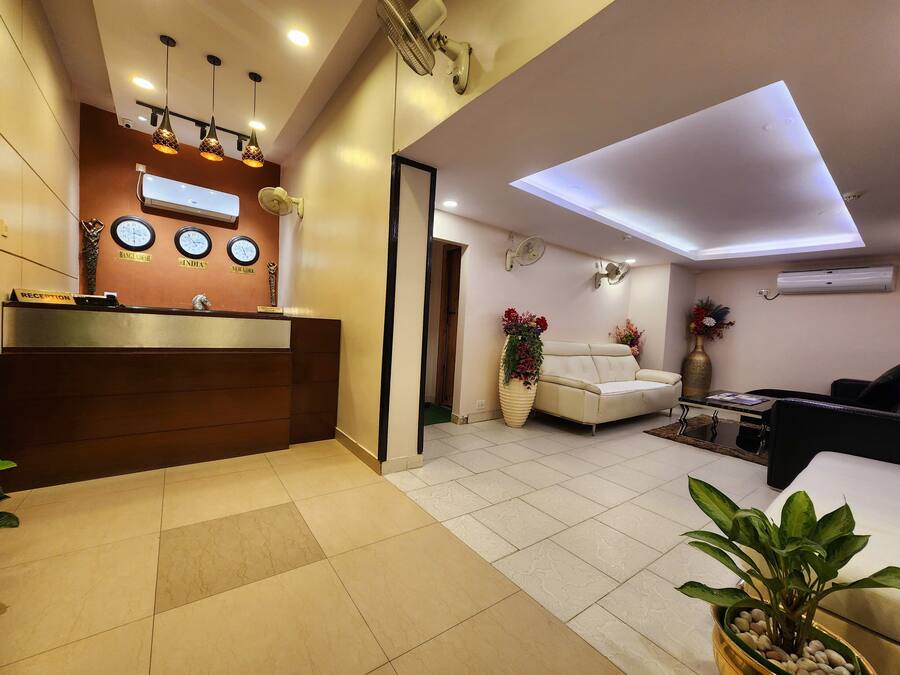 A hotel reception area with a reception desk, wall clocks, and a seating area with a sofa and chairs.