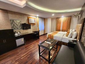 Ein Hotelzimmer mit Holzboden, einem Bett mit weißer und beiger Bettwäsche, einem Schreibtisch, einem Flachbildfernseher, einer Kaffeemaschine und einem kleinen Kühlschrank.