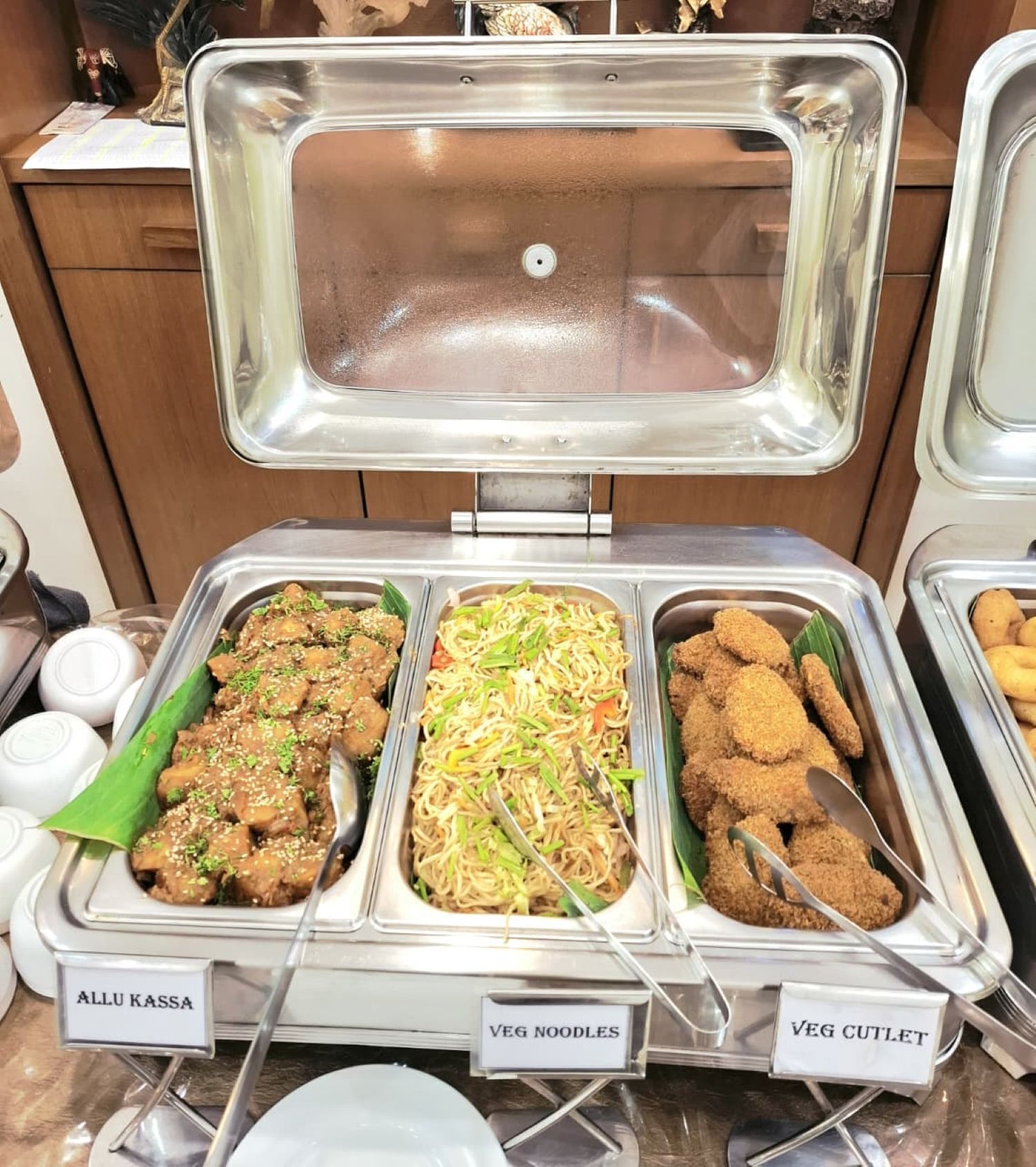 A buffet with labeled sections for allu kassa, veg noodles, and veg cutlet.