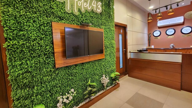 A reception area with a green wall, a TV mounted on it, and a wooden reception desk. - HOTEL HOUSEZ43 (Kolkata)