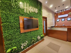 A reception area with a green wall, a TV mounted on it, and a wooden reception desk. - HOTEL HOUSEZ43 (Kolkata)