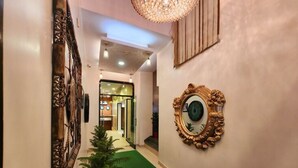 A hallway with a green carpet, a large mirror with an ornate frame, and a decorative wall piece. - HOTEL HOUSEZ43 (Kolkata)