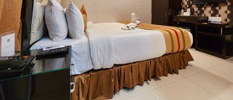 Quarto de hotel com cama, escrivaninha com computador, televisão e guarda-roupa.