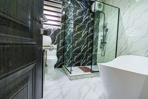 A modern bathroom with a glass-enclosed shower, a white bathtub, and a dark wooden door.