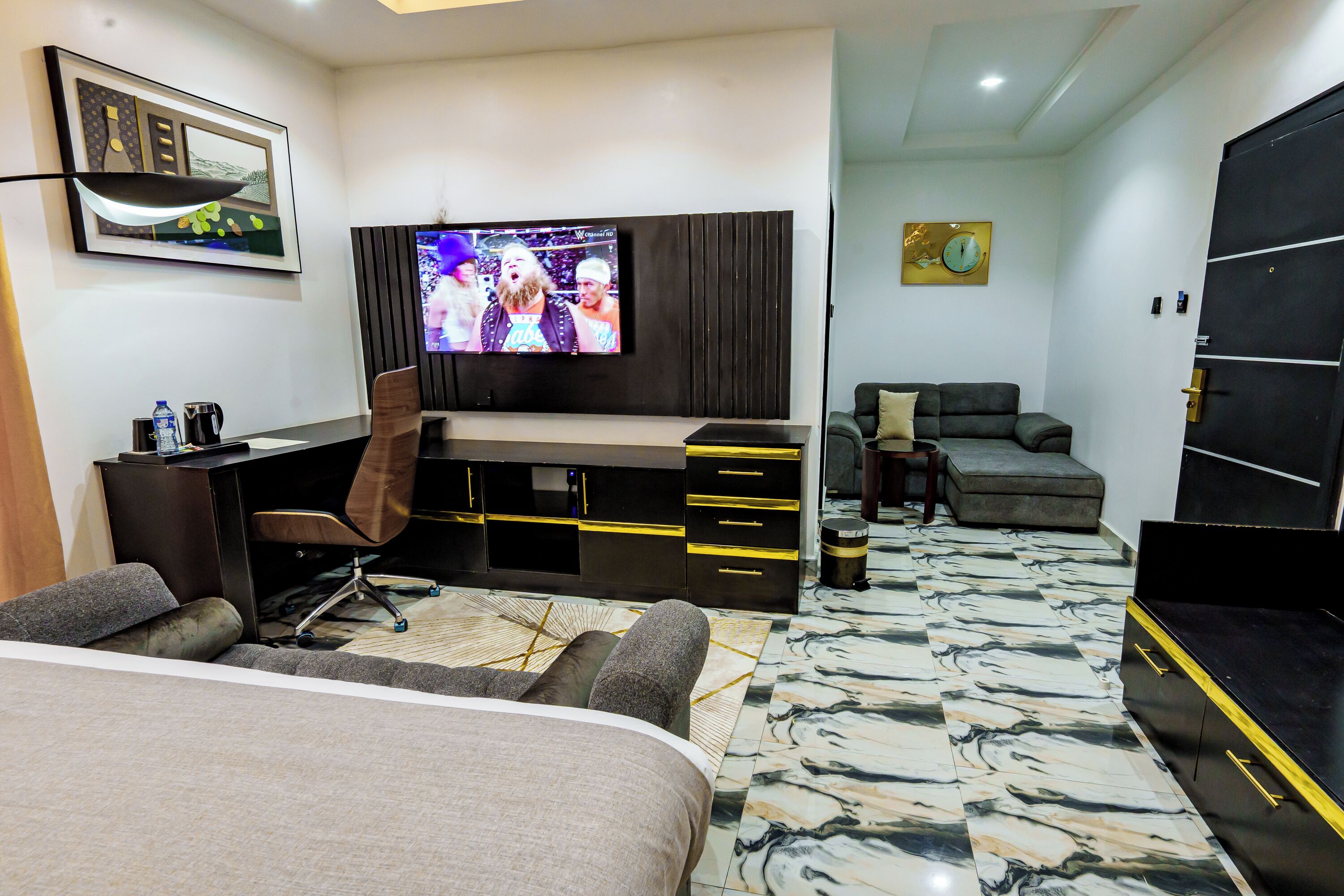A modern hotel room with a bed, a desk, a television, and a seating area.
