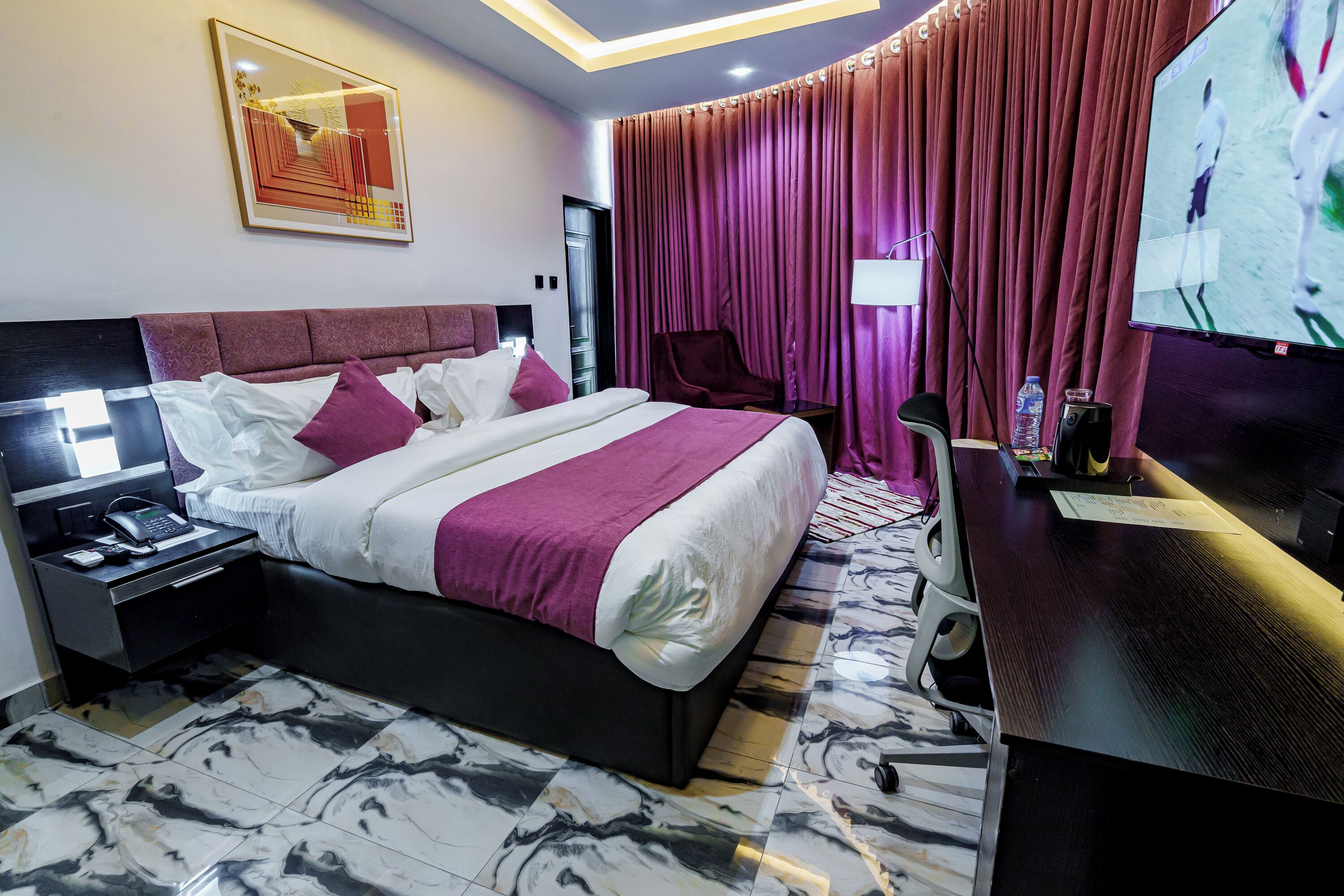 A hotel room with a bed, a desk, a chair, a TV, and a nightstand.