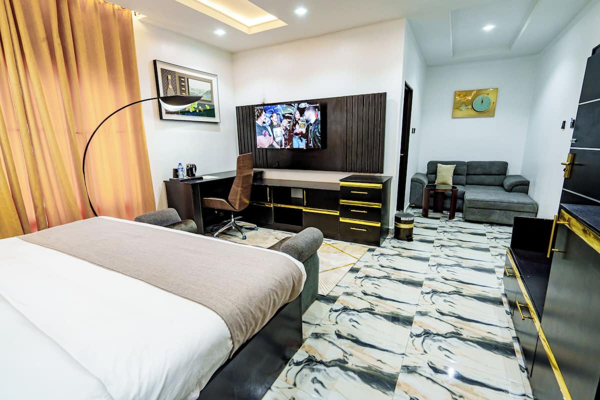 A modern hotel room with a large bed, a desk with a chair, a sofa, a TV, and a wardrobe.