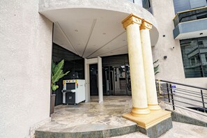 Entrada de un edificio con suelo de mármol, mostrador de recepción y una escalera con barandilla.