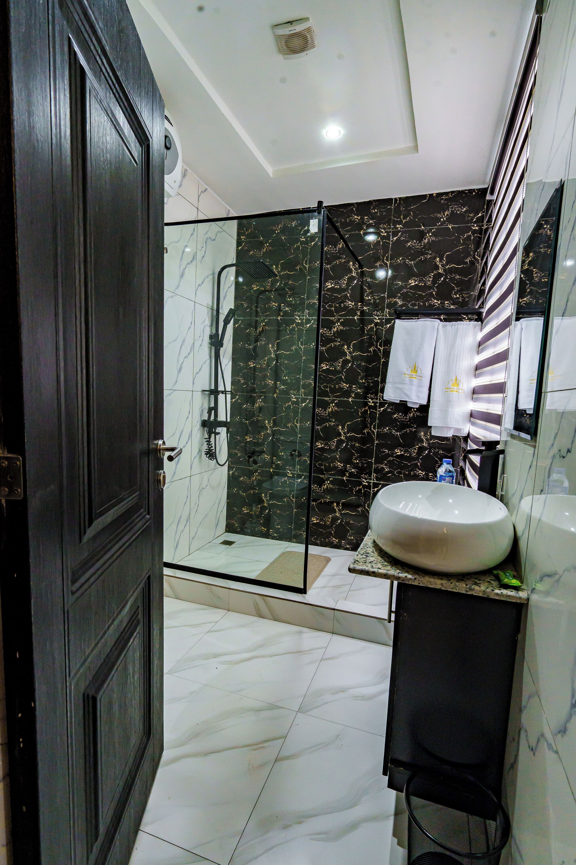 A modern bathroom with a glass-enclosed shower, a marble-tiled floor, and a large sink.