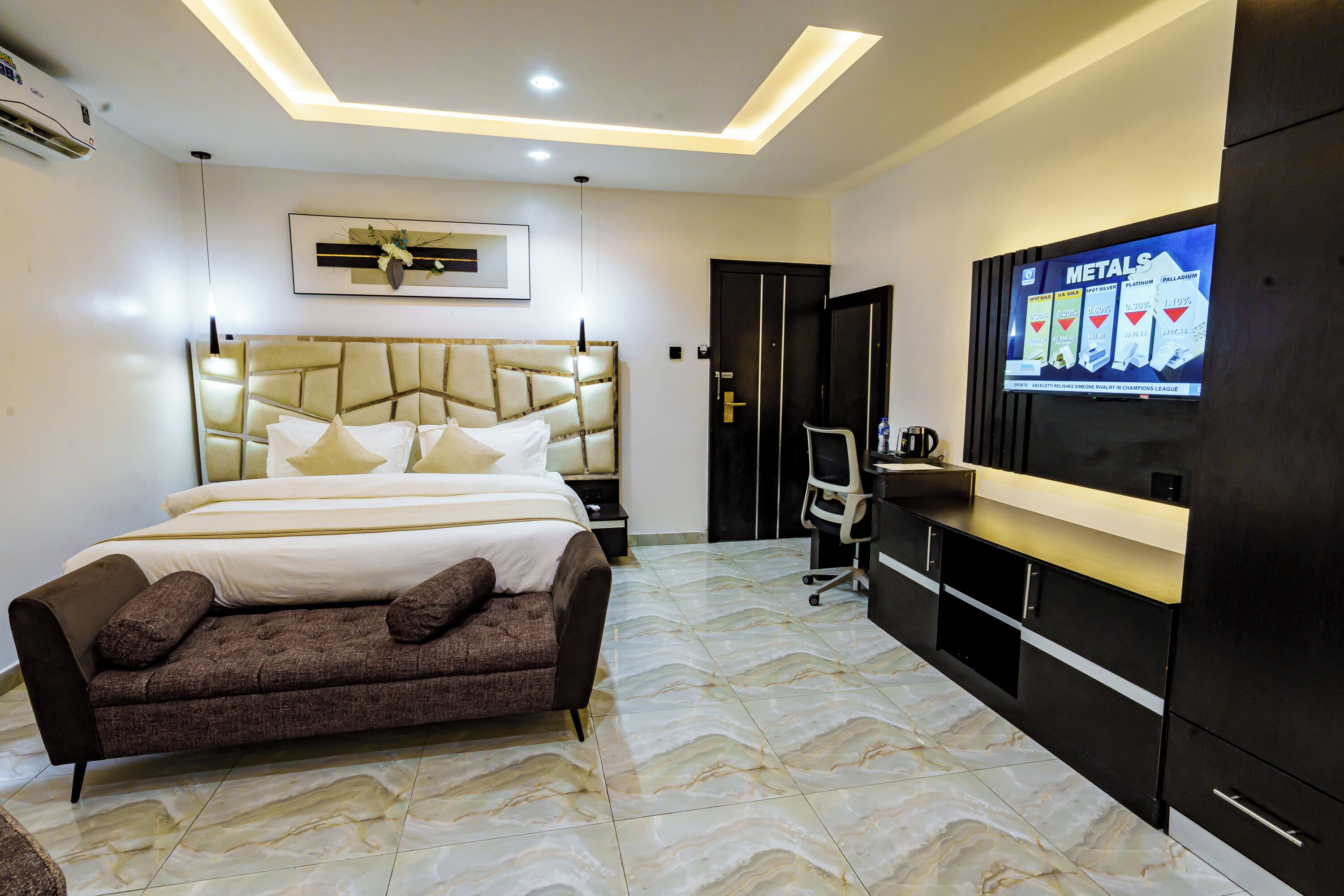 A modern hotel room with a large bed, a sofa, a desk, and a television displaying an advertisement.