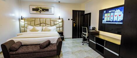 A modern hotel room with a large bed, a sofa, a desk, and a television displaying an advertisement.