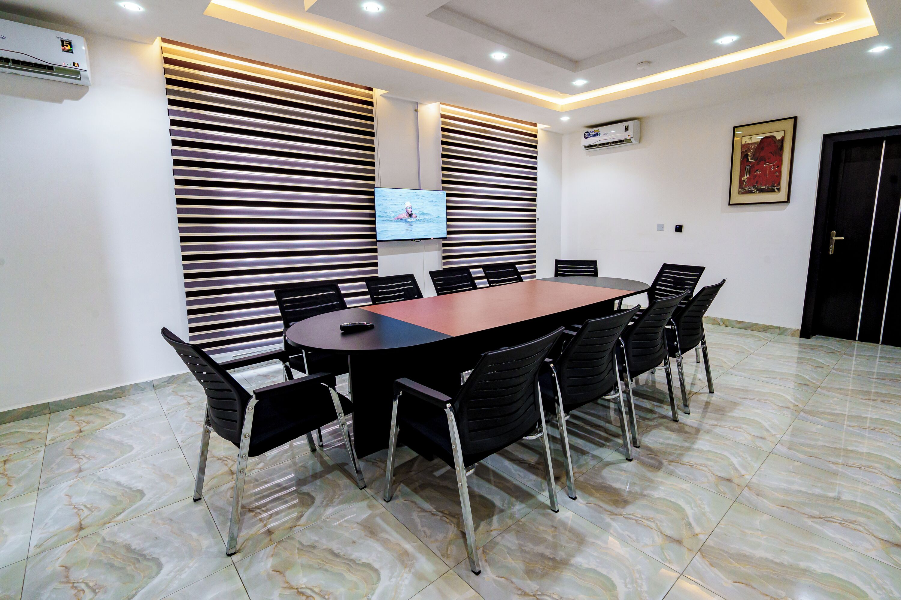 A conference room with a long table, black chairs, and a TV screen.