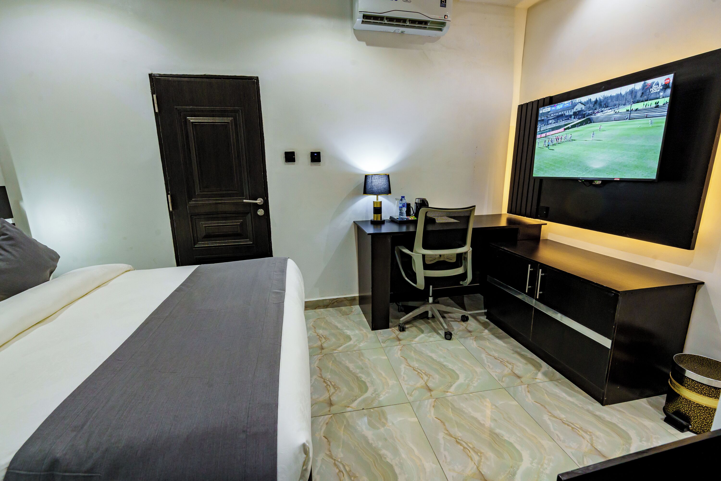 A hotel room with a bed, a desk with a chair, a television, and a cabinet.