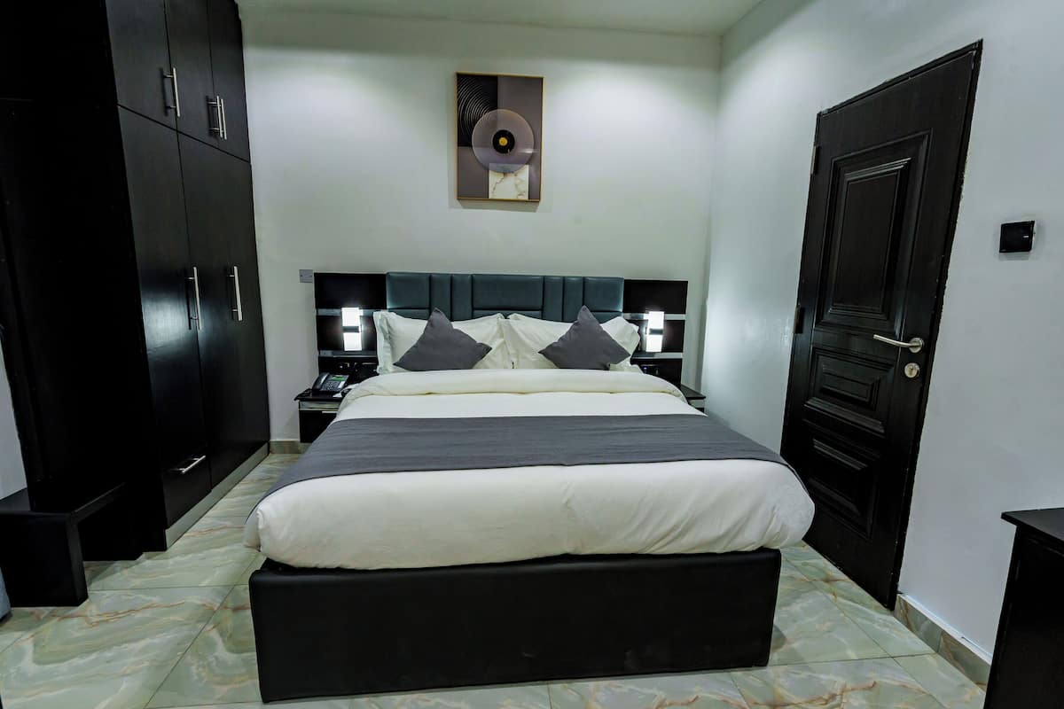 A bedroom with a large bed, dark wardrobe, bedside tables, and a wall-mounted artwork.