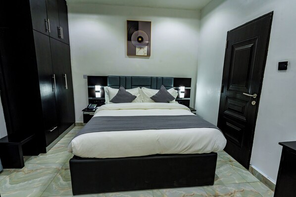 Un dormitorio con una cama grande, un armario oscuro, mesitas de noche y una obra de arte colgada en la pared.