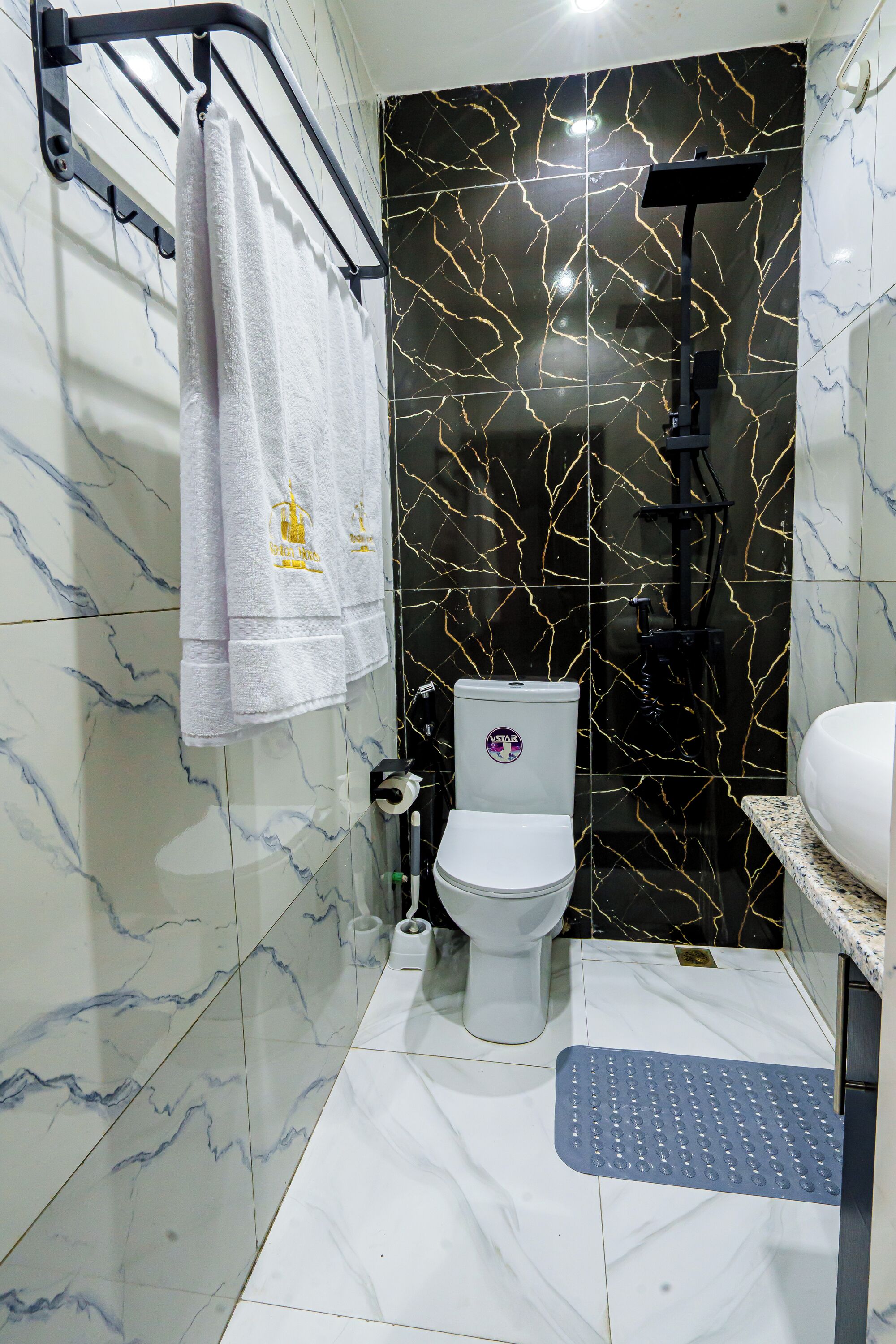 A bathroom with a toilet, a towel rack with towels, a shower head, and a step for accessibility.
