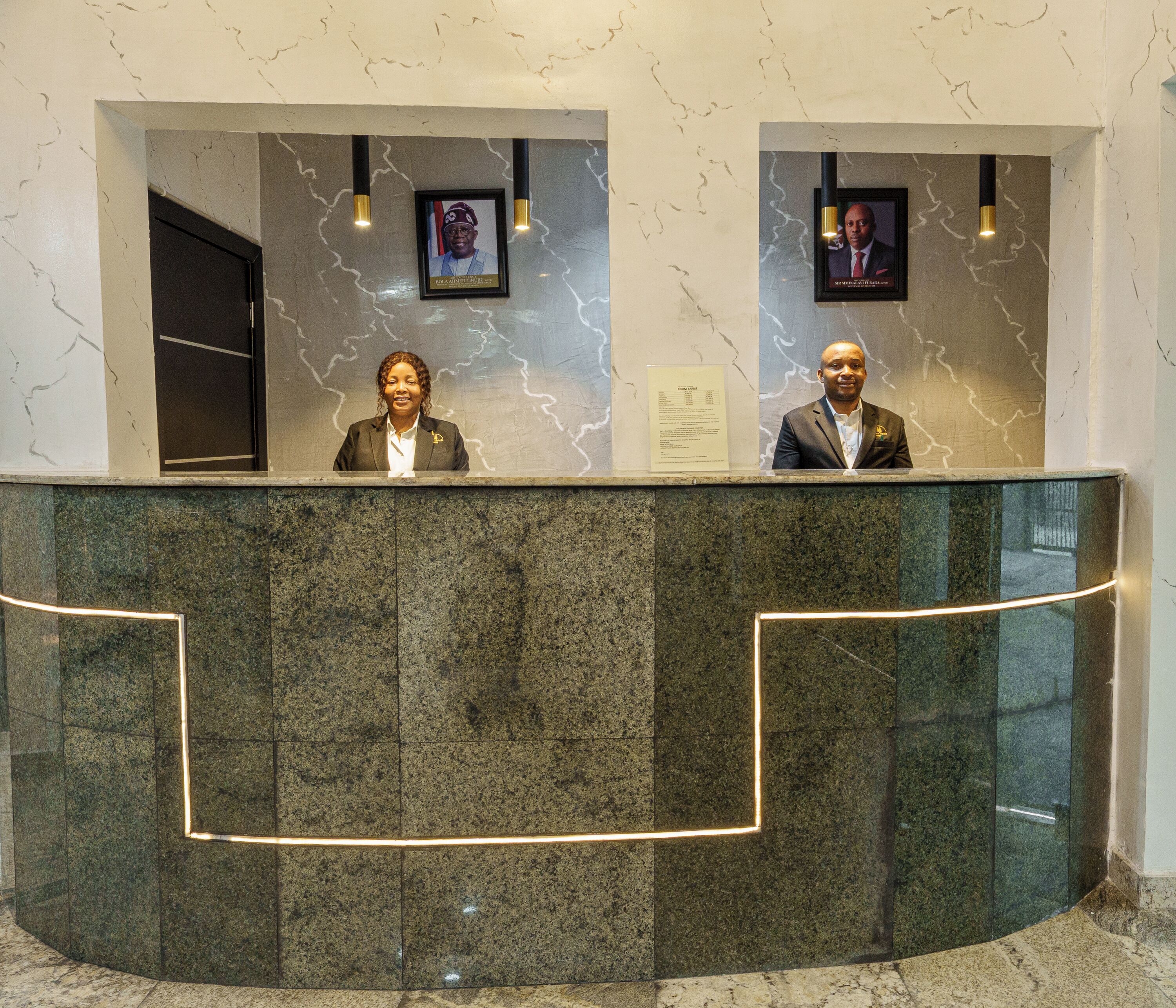 A reception desk with two framed portraits above it, a marble wall with a lightning pattern, and a glass partition.