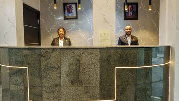A reception desk with two framed portraits above it, a marble wall with a lightning pattern, and a glass partition.