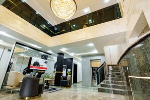 A modern lobby with a high ceiling, a chandelier, a staircase, and a reception desk. - Roston Hotels (Port Harcourt)