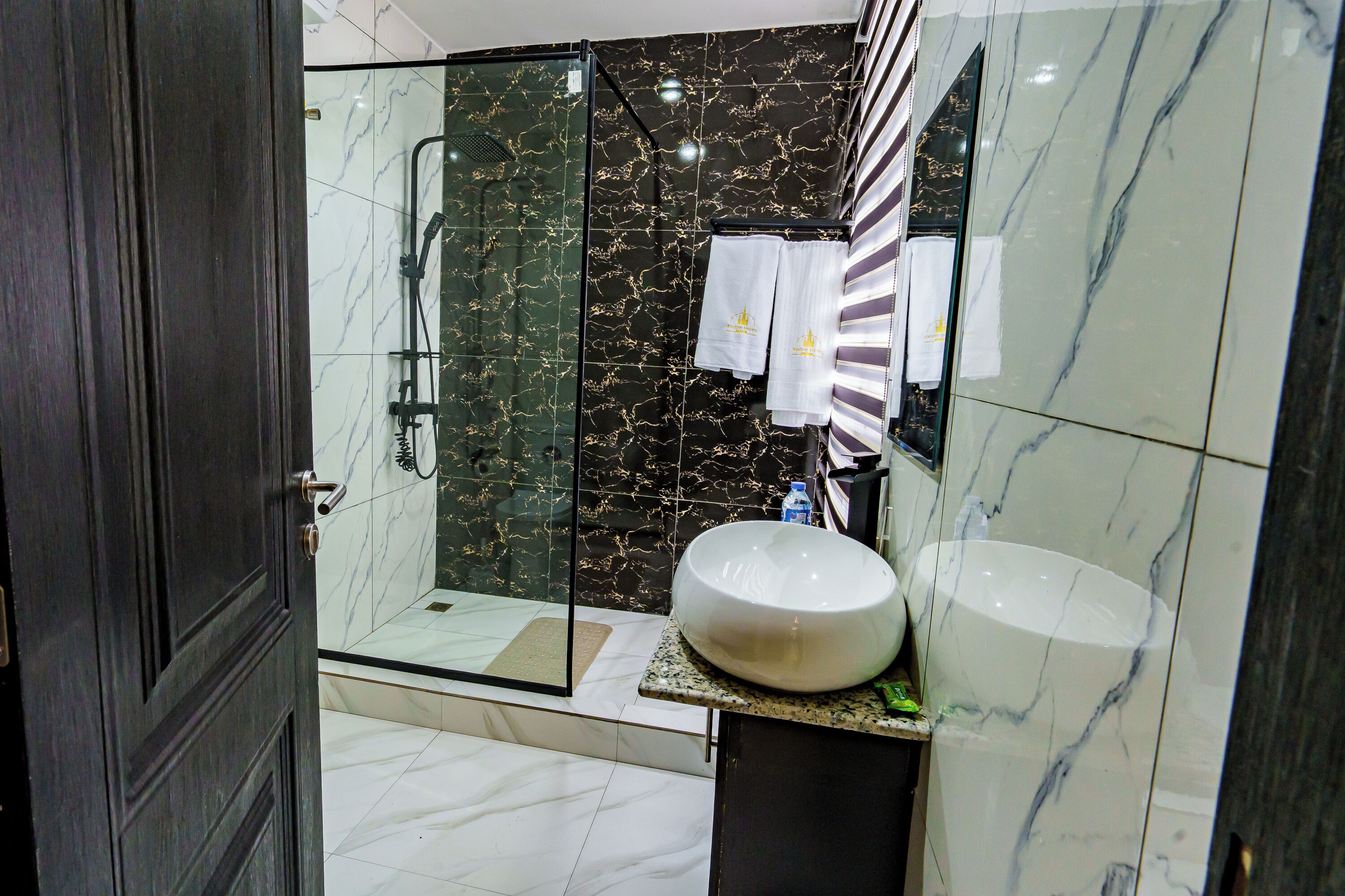 Un baño moderno con ducha de vidrio, un lavamanos grande de mármol y una pared de mármol oscuro.
