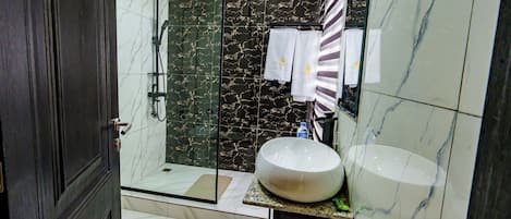 Un baño moderno con ducha de vidrio, un lavamanos grande de mármol y una pared de mármol oscuro.