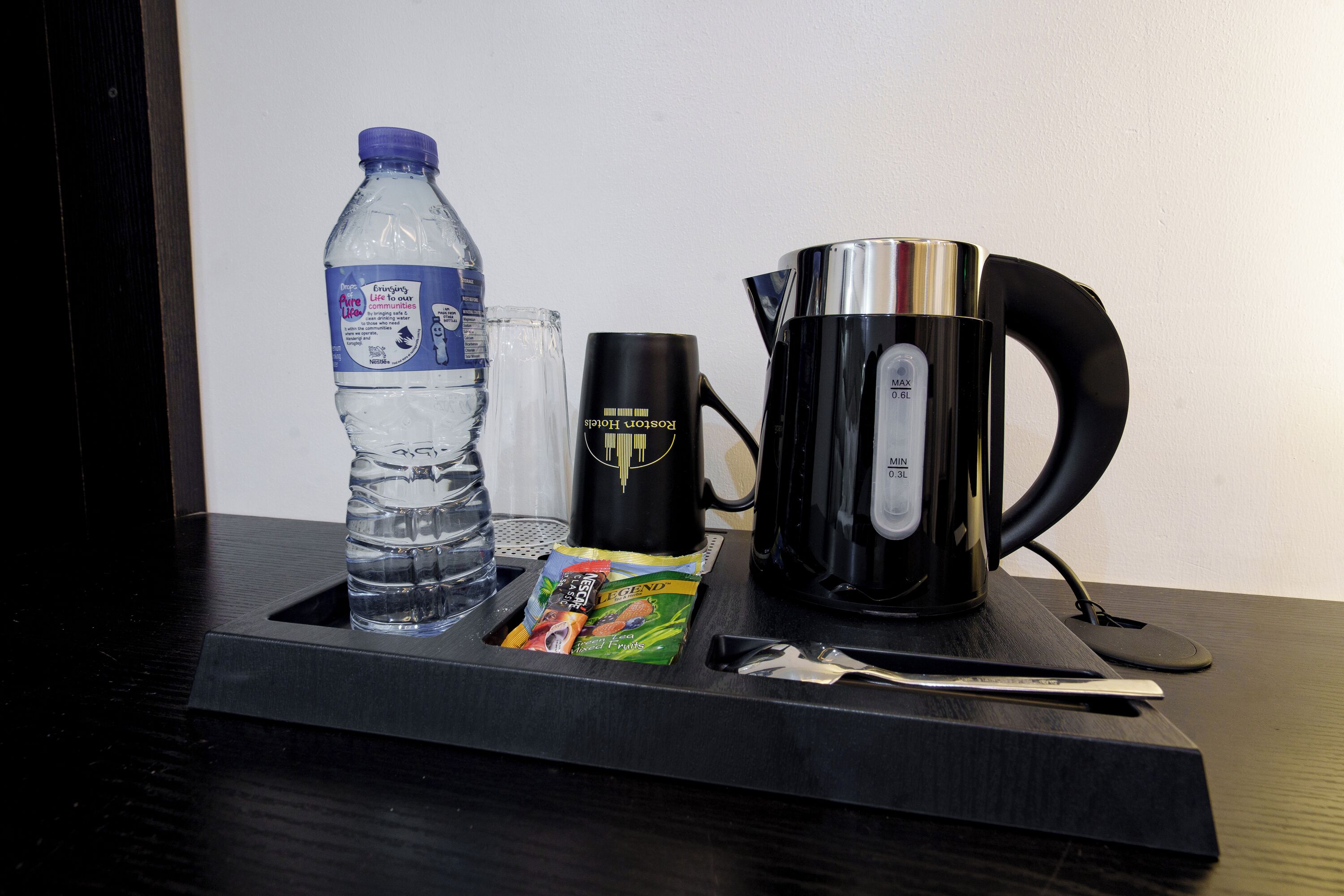 Una bandeja con una botella de agua, una taza de café, un paquete de bocadillos y una cuchara.