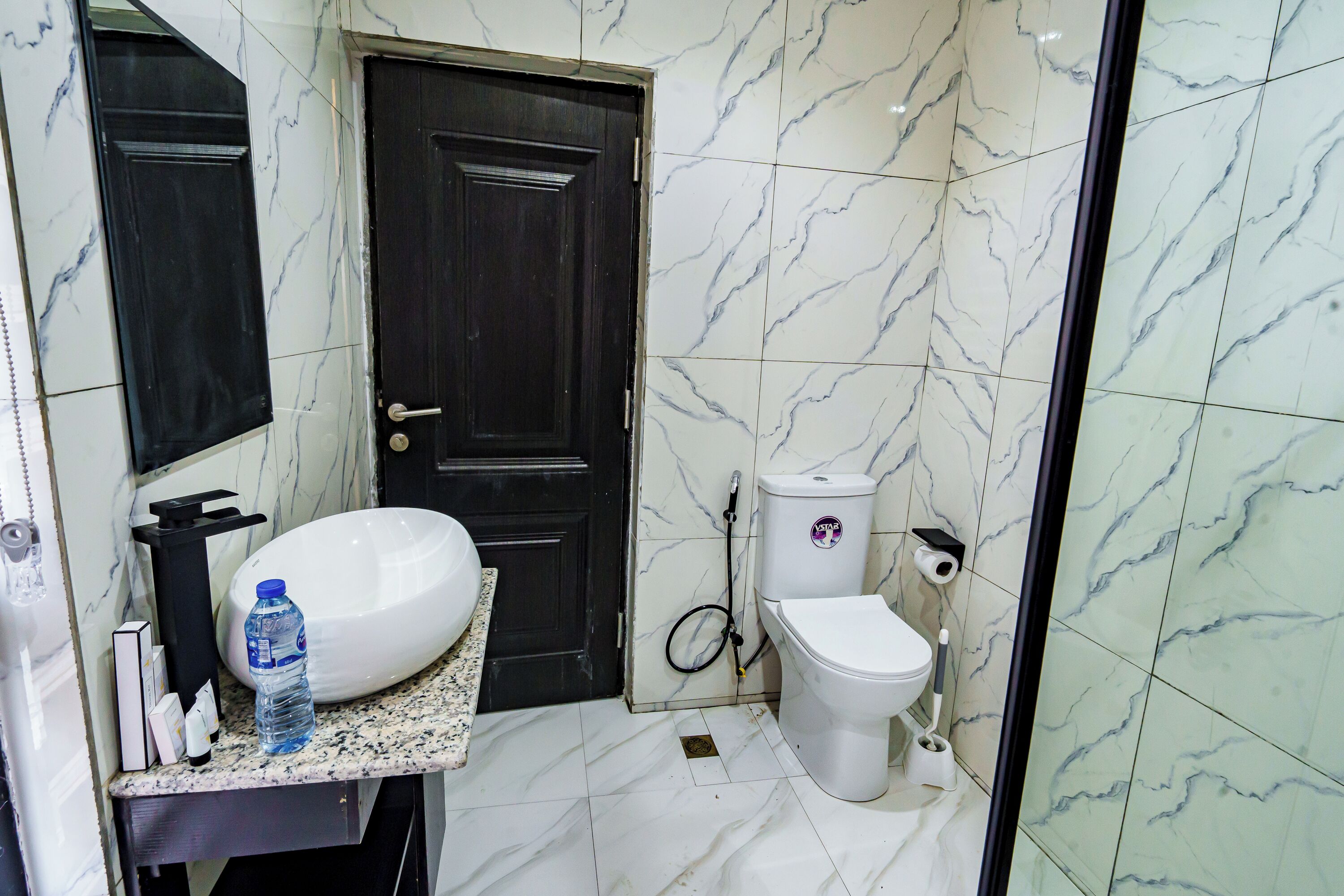 A bathroom with a white sink, dark door, toilet, and marble tiles.