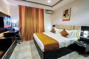 Habitación de hotel con cama, escritorio, silla, televisor, aire acondicionado y un cuadro en la pared.