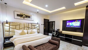 A modern hotel room with a large bed, a sofa, a TV, and a desk. - Roston Hotels  (Port Harcourt)