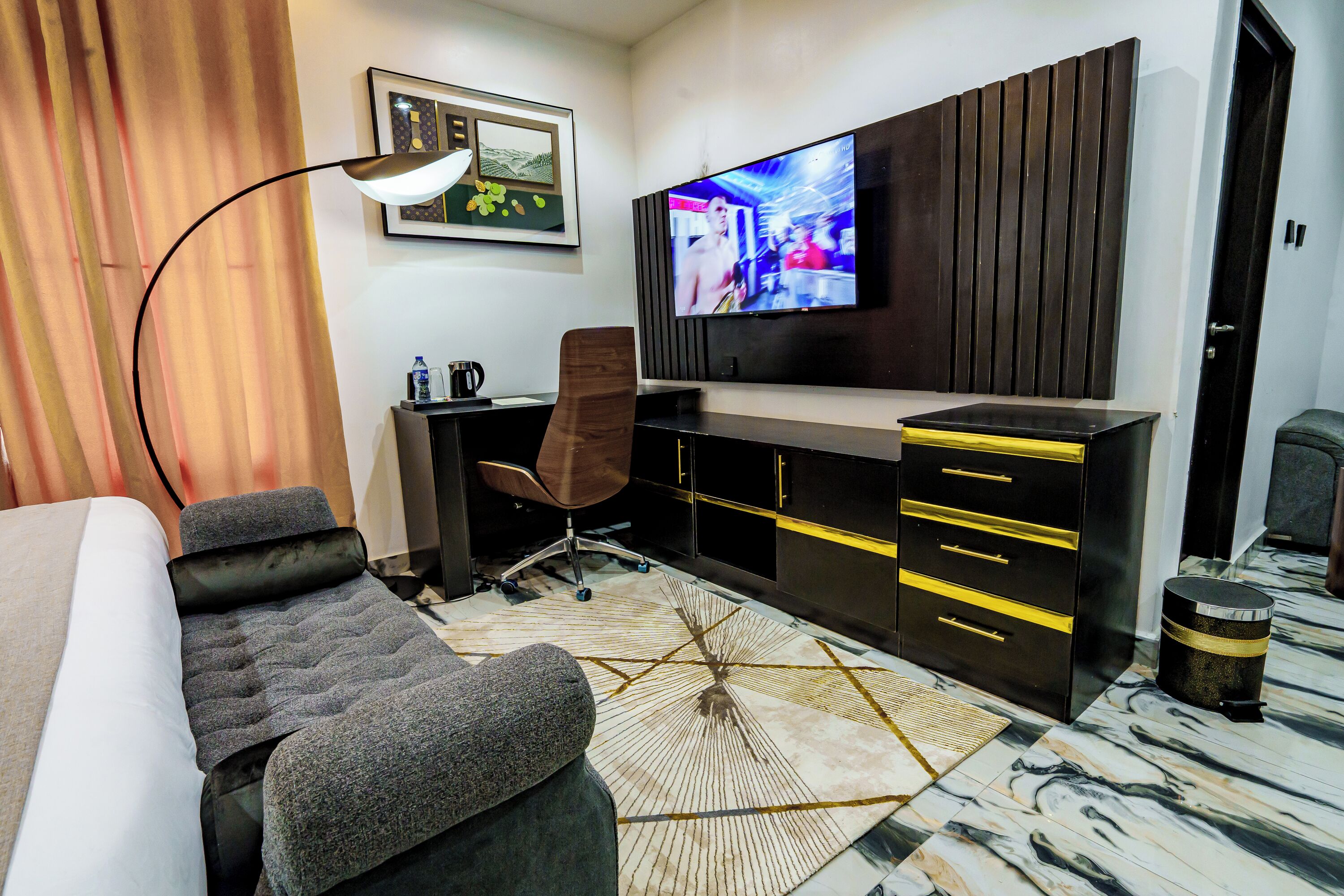 A modern hotel room with a large bed, a desk with a chair, a television, and a patterned rug.