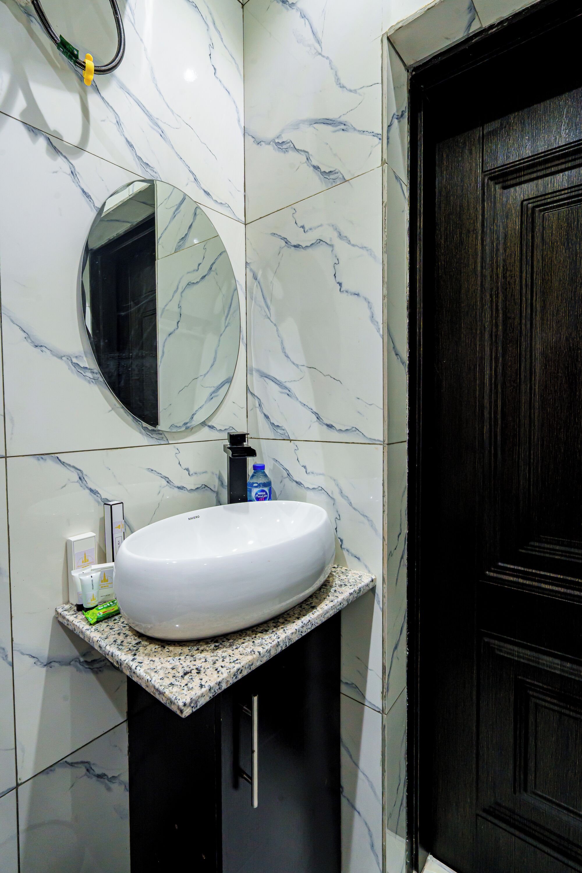 Une salle de bain avec un lavabo en marbre blanc, un miroir rond et une porte en bois foncé.
