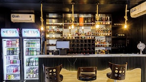 A bar area with two refrigerators labeled 'NEXUS', a bar counter with bottles, and three stools. - Roston Hotels  (Port Harcourt)